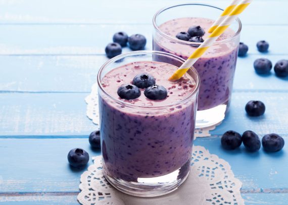 two glasses of blueberry smoothie on blue colored wooden table