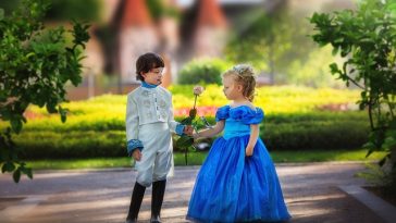 zwei Kinder verkleidet als Prinzessin und Prinz in einem Park.